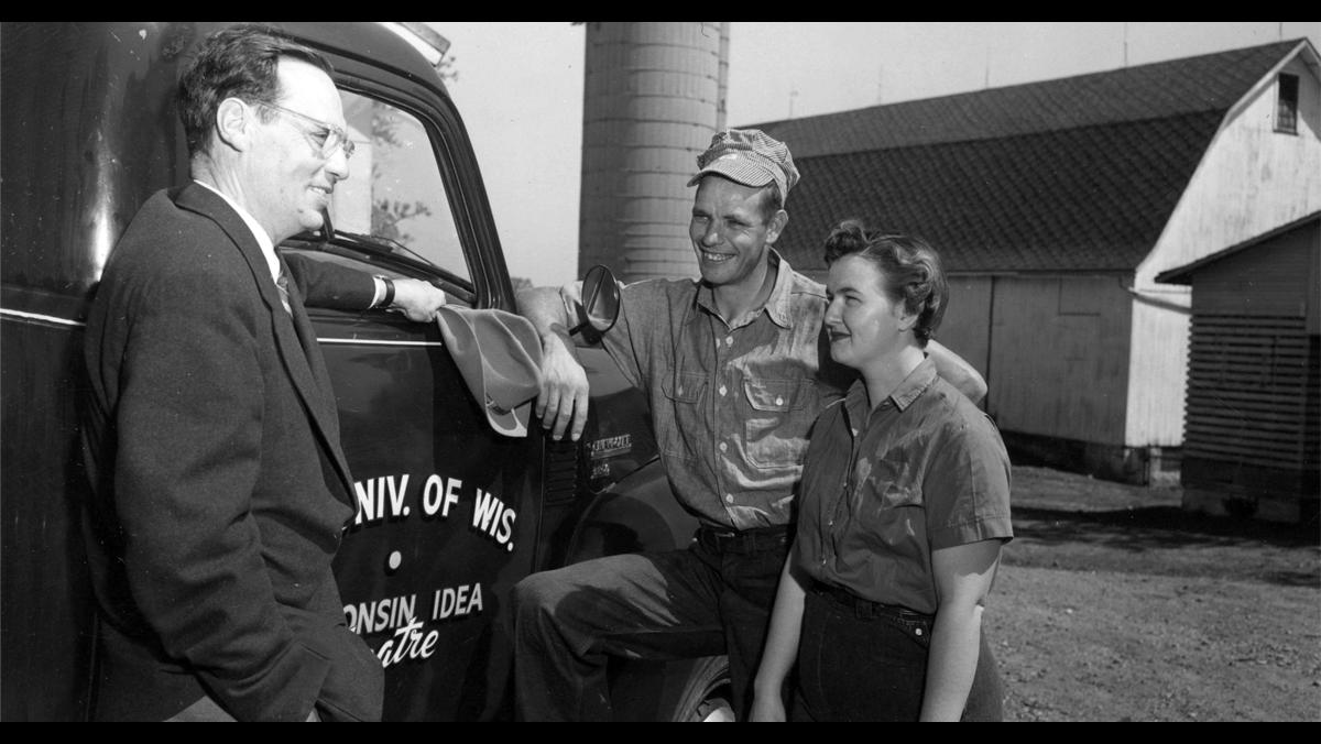 Robert Gard visits with farmers on May 9, 1955. Gard traveled across the state (note the Wisconsin Idea Theater logo painted on the side of his truck) to promote and cultivate the theatrical arts in rural communities. Gard was a well-known figure in Wisconsin through his travels as well as his WHA-Radio program, and later WHA-TV program, “Wisconsin Is My Doorstep.”  UW Digital Collections/ID S15183